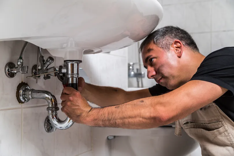 A plumber works on pipes